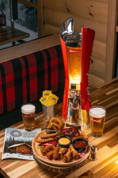 A beer tower, two beers, and a platter of pub-style appetizers on a wooden table.