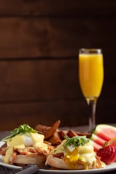 Eggs Benedict with crispy bacon, fresh fruit, and a tall glass of orange juice.